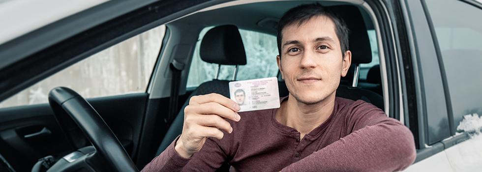 young man sitting in car holding license